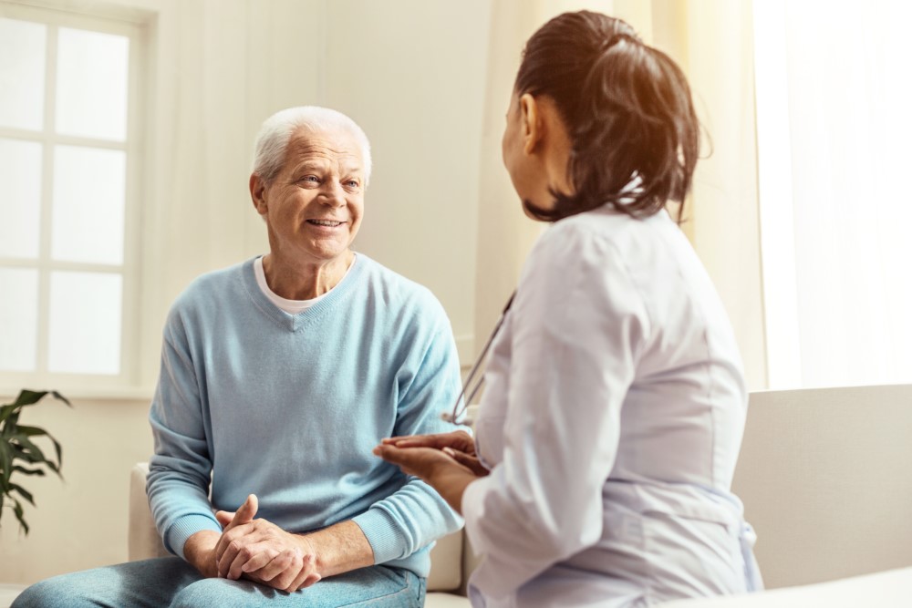 Pleasant communication. Positive cheerful senior man smiling and looking at the nurse while having a conversation with her