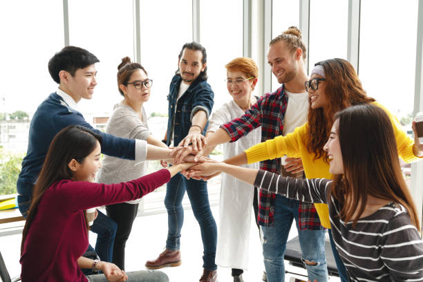 Multiethnic young team stack hands together as trusted unity and teamwork in modern office. Diverse group togetherness collaboration or friends huddle concept. Power of startup business team building.