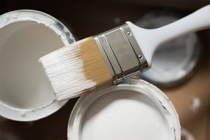 White paint and a brush as you need to complete home improvement before listing your Virginia home.