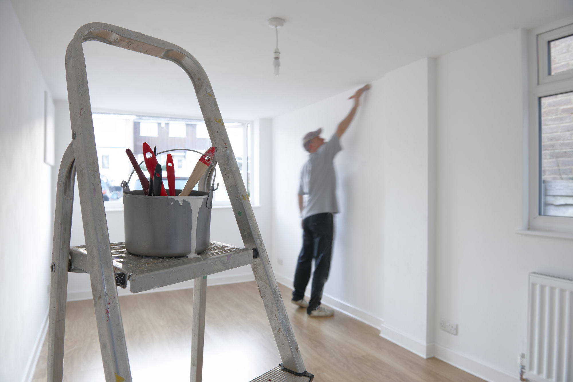 Man decorating a room with ladder and paint pot in foreground