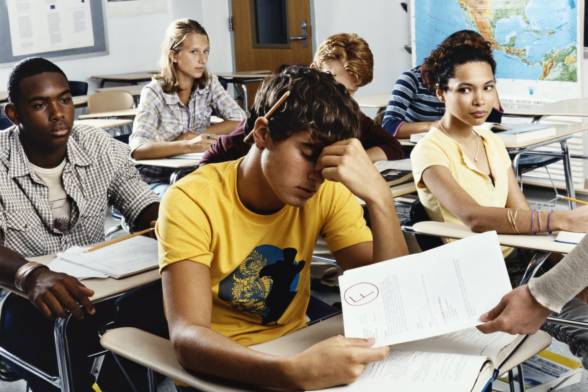 Teenage Boy Sits Looking Down in Embarrassment as he is Given a Failed Exam Paper