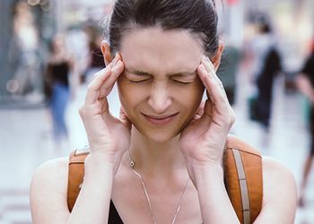 Portrait of a young frustrated girl standing in the crowd, headache or anxiety attack, city life problems